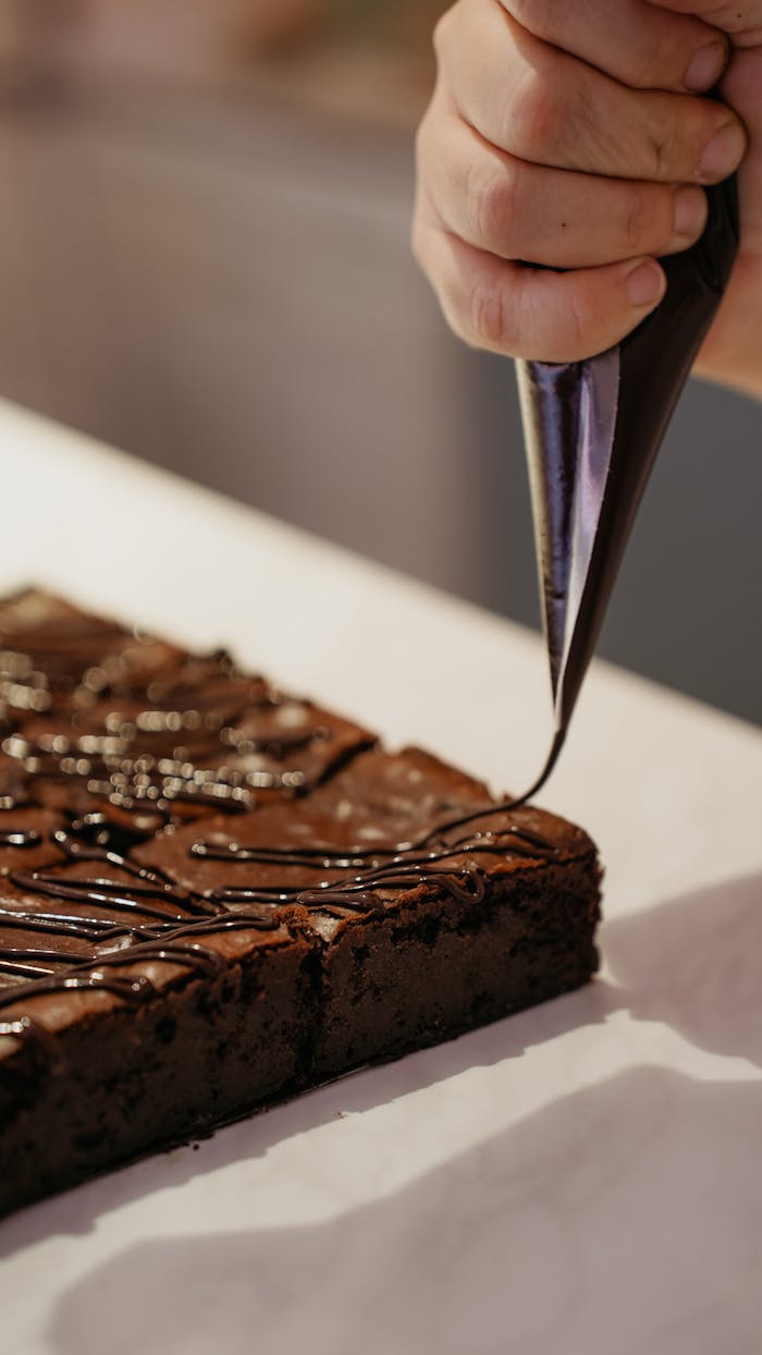 Hand decorates delicious chocolate brownie with icing for dessert.